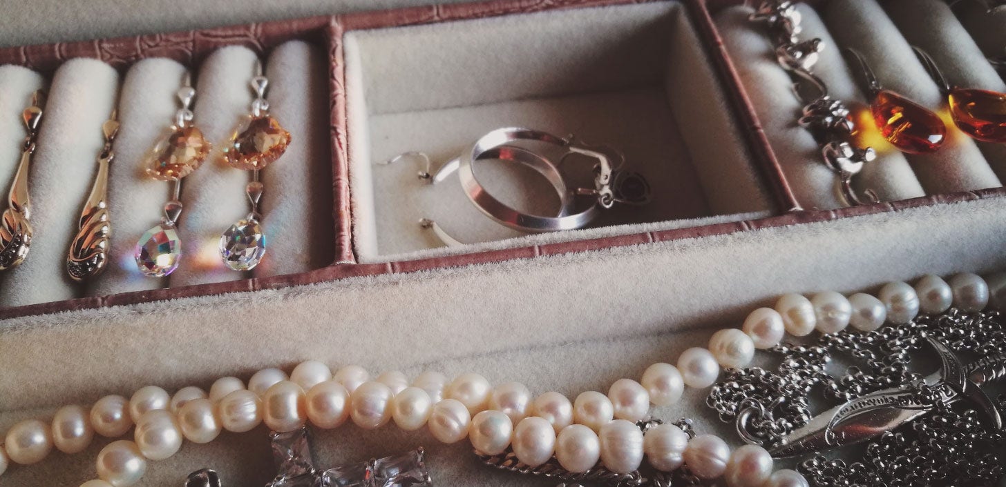 A jewelry box with earrings, rings and a pearl necklace.
