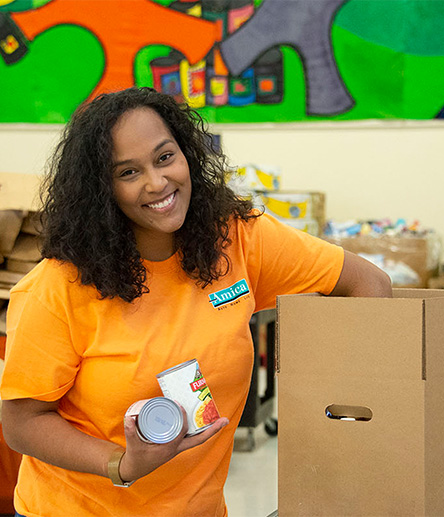 Amica volunteer smiling while packing canned goods in a cardboard box.