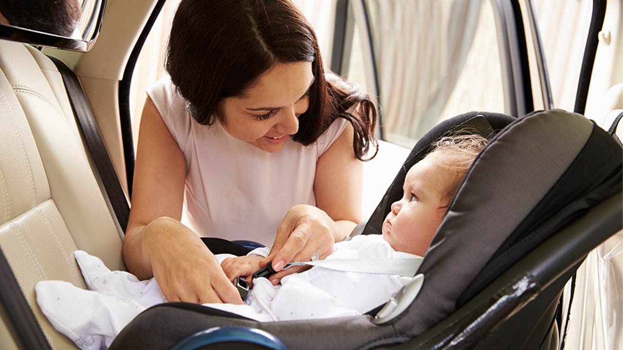 Mom leaning into the back seat of her car buckling her infant into a car seat