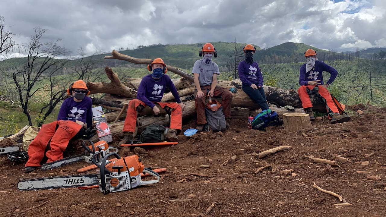 Five volunteers sit on a log after cleaning up areas affected by the California wildfires.