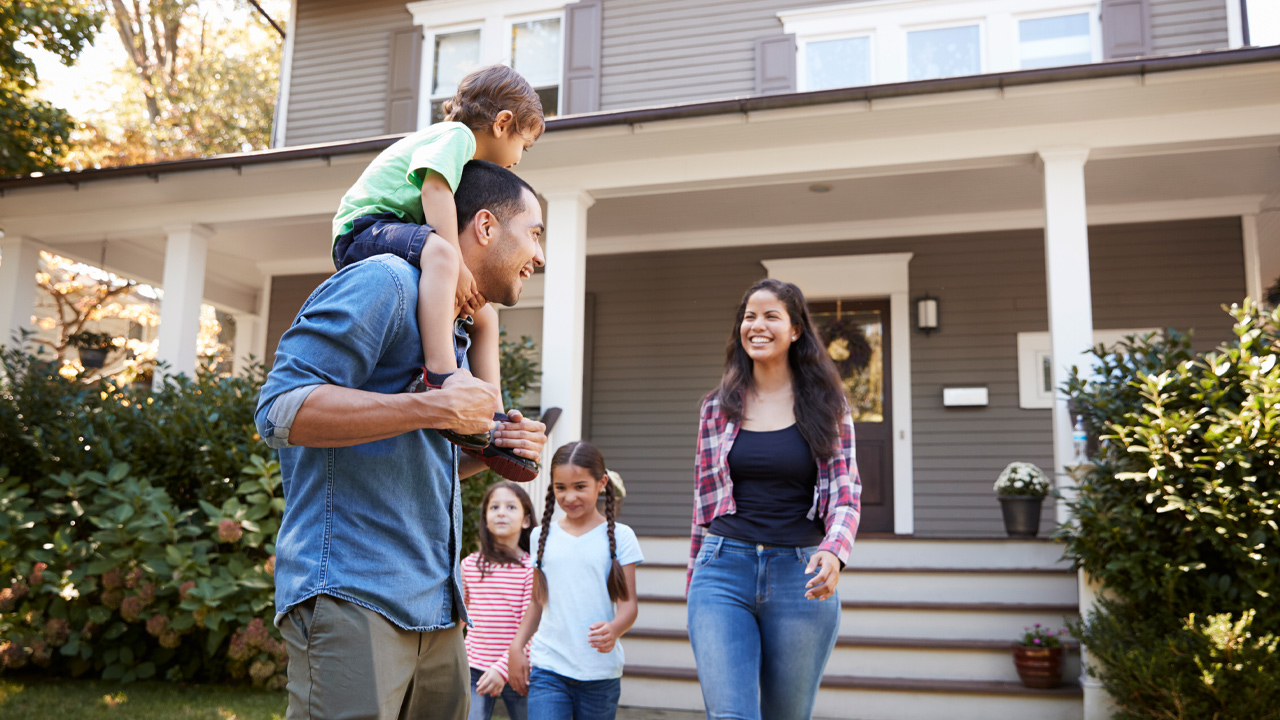 Man with child on shoulders, 2 small children and woman in front of home