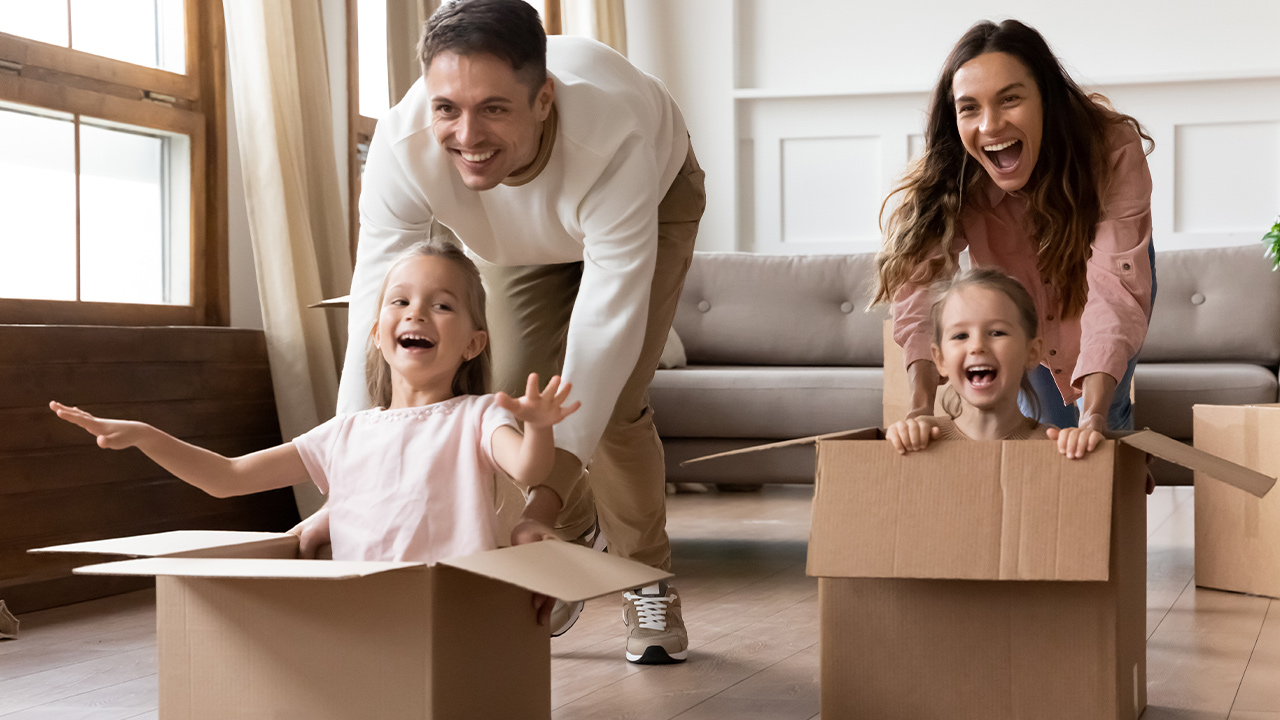 A man and woman push two little girls in cardboard boxes.