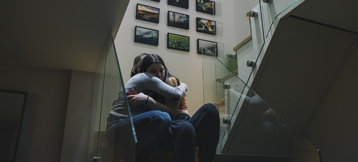 Two people embracing each other while sitting in a dimly lit stairwell