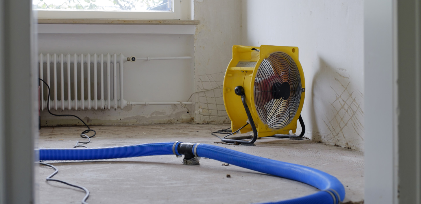 A room with a drainage hose and industrial fan to remove water.