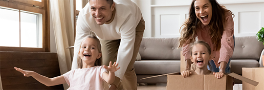 Smiling man and laughing woman push laughing children in cardboard boxes